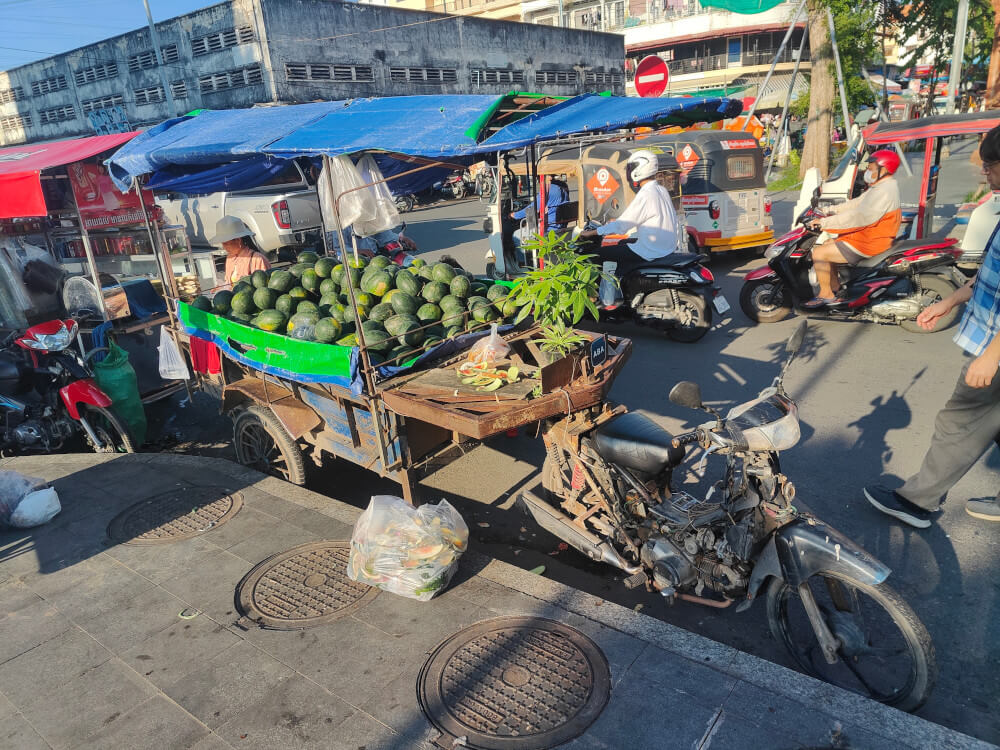 A huge container full of watermelons attached to a motorbike